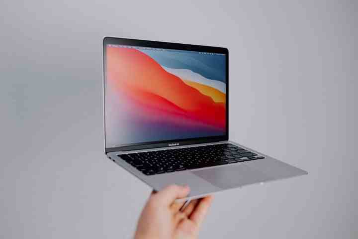 Eine Person hält ein MacBook Air vor einem grauen Hintergrund.