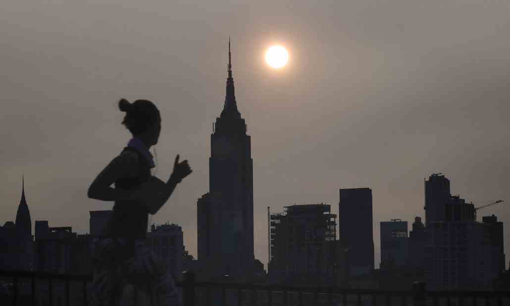 a photo of a hazy New York skyline and a woman jogging past in silhouette