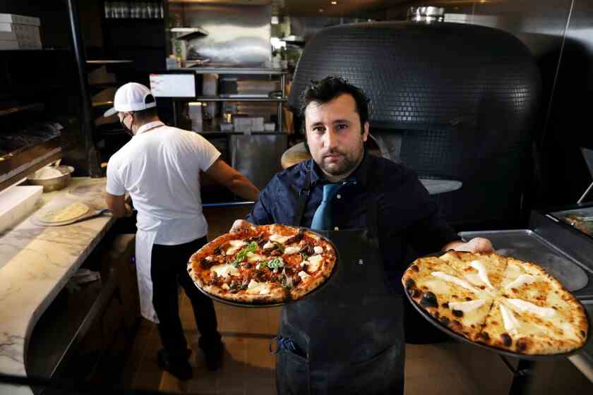 Ein Foto von Küchenchef Daniele Uditi, der vor seinem Pizzaofen steht und zwei ganze Pizzen in die Kamera hält.