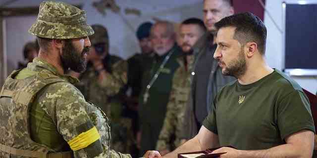 Auf diesem Foto, das am Samstag, den 18. Juni 2022 vom Presseamt ​​des ukrainischen Präsidenten zur Verfügung gestellt wurde, überreicht der ukrainische Präsident Wolodymyr Selenskyj (rechts) einen Militärangehörigen, als er die vom Krieg heimgesuchte Region Mykolajiw besucht. 