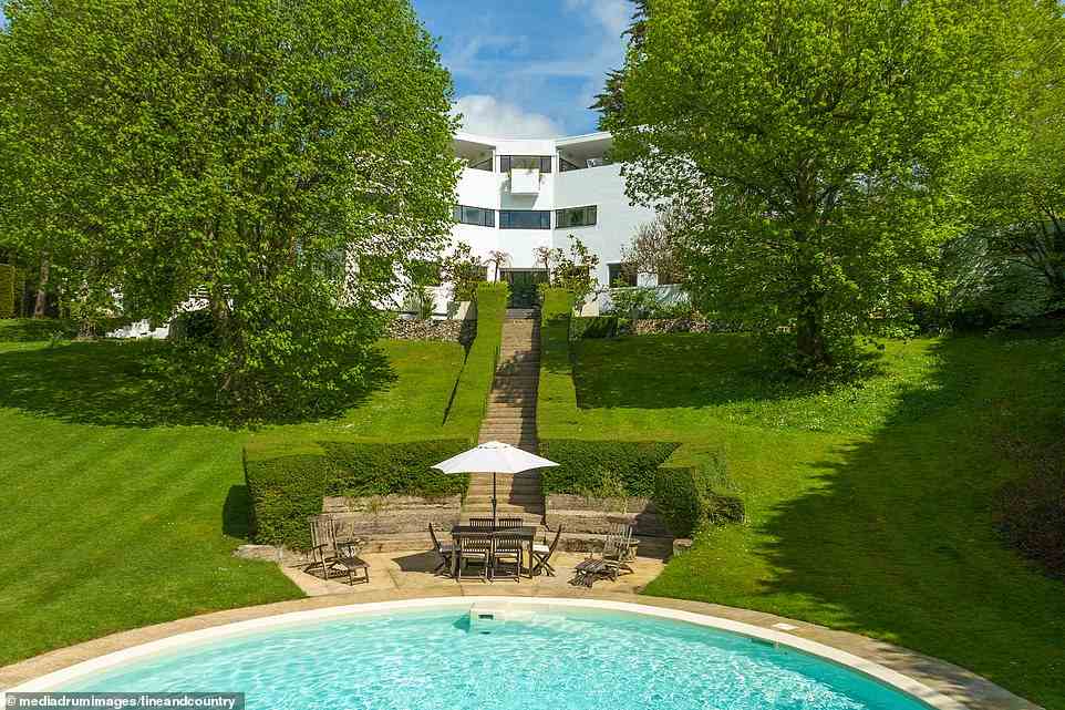 The 1929 Grade II listed home made up of modernist architecture rests on 1.7 acres of gardens, has a detached garage and 1,000sq feet of part-covered roof terrace. Pictured, the gardens and swimming pool with a dedicated staircase to the house