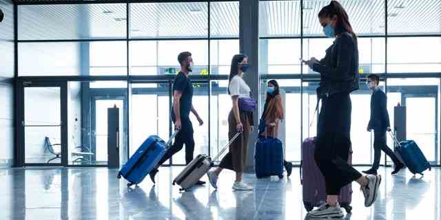 Menschen, die während der Coronavirus-Pandemie mit dem Flugzeug reisen, werden mit Gesichtsmasken gezeigt, während sie durch ein Flughafenterminal gehen. 