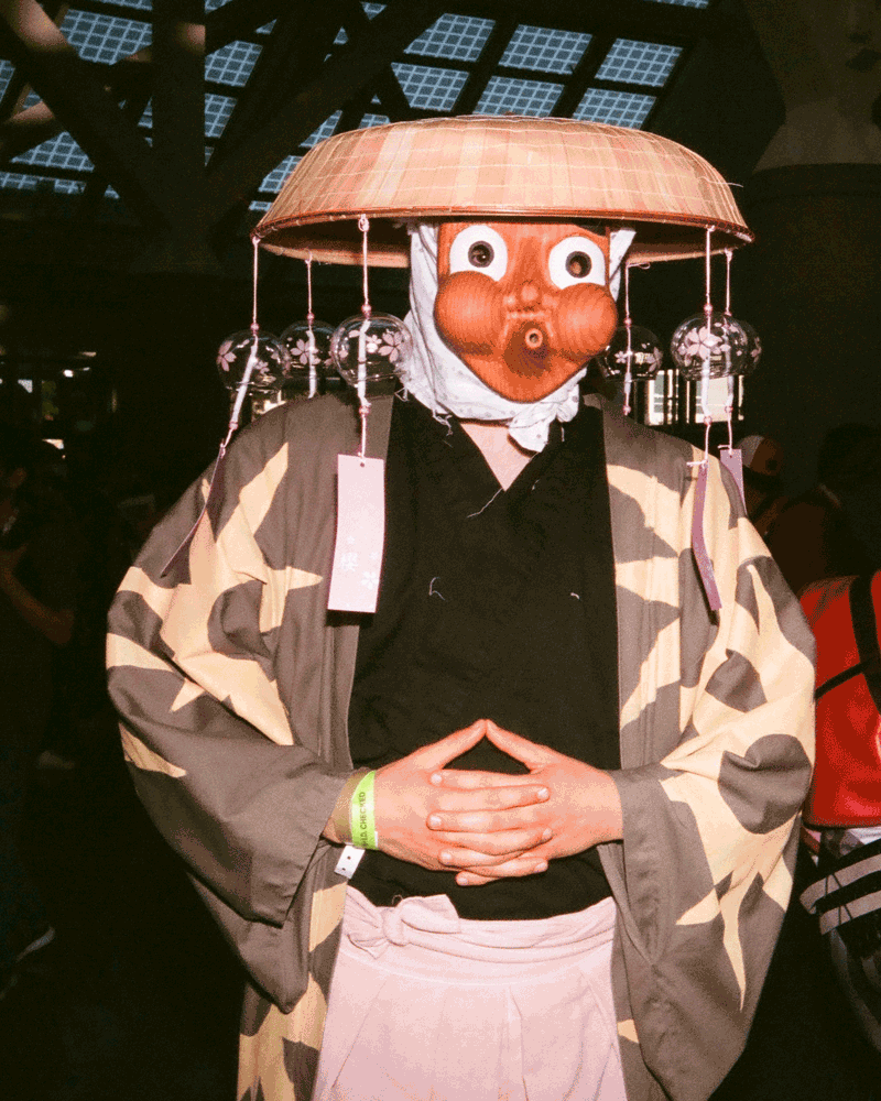 Ein Gif einer Person, die einen Kimono und einen Holzhelm und eine Gesichtsmaske mit aufgeblasenen Wangen trägt
