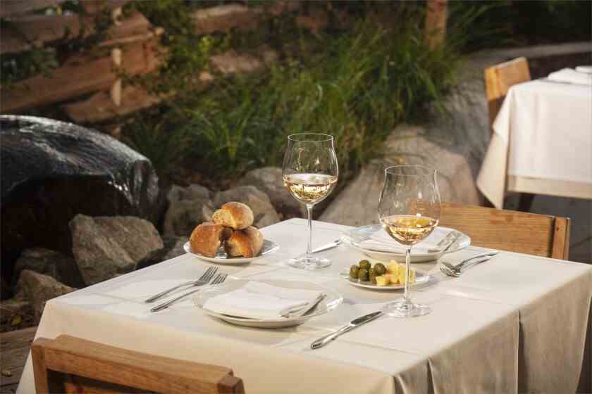 Ein Foto von einem Tisch für zwei mit eingeschenkten Gläsern Weißwein und einem Teller Oliven mit Butter und einem Brotkorb.
