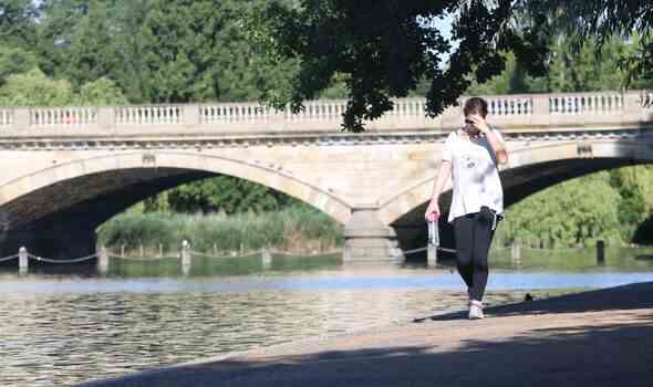 Eine Dame schützt ihr Gesicht vor der Sonne beim Gehen im Hyde Park, London