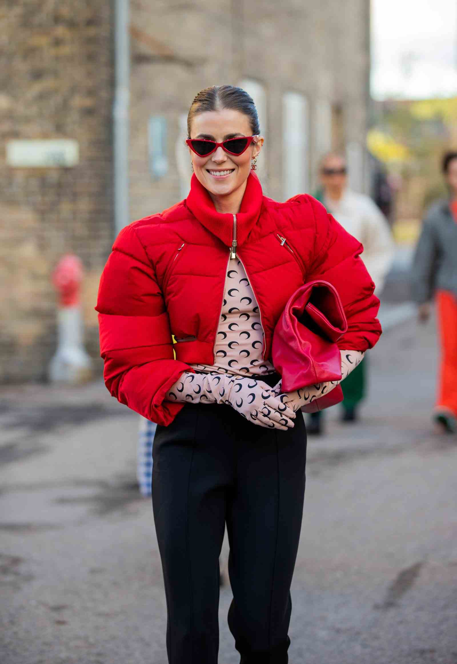 Nina Sanbech ist draußen bei der Copenhagen Fashion Week und trägt einen roten Daunenmantel, dessen Haare zu einer glatten Hochsteckfrisur zurückgebunden sind.