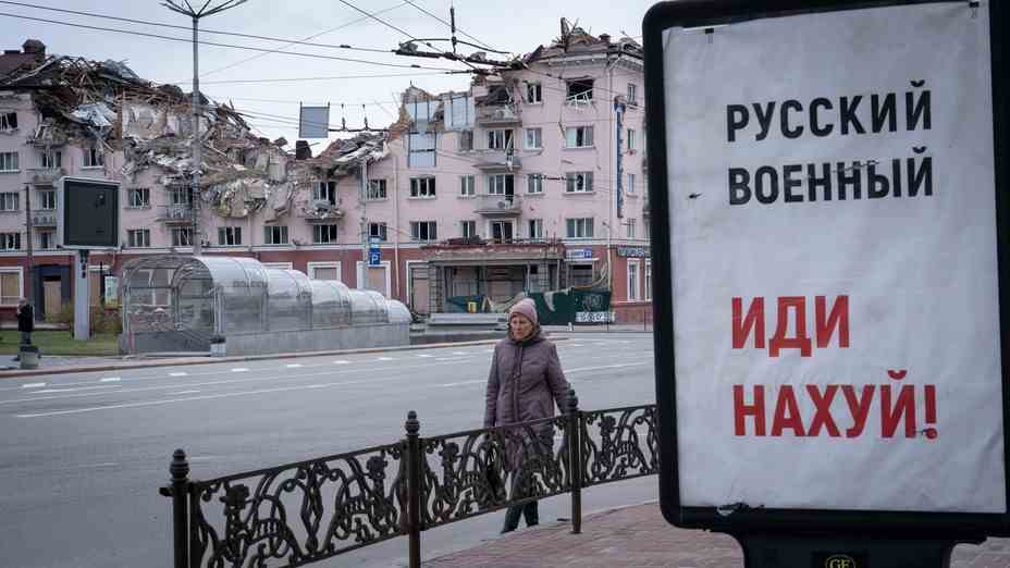 A board in Russian in the foreground, against a bombed-out building in the background.