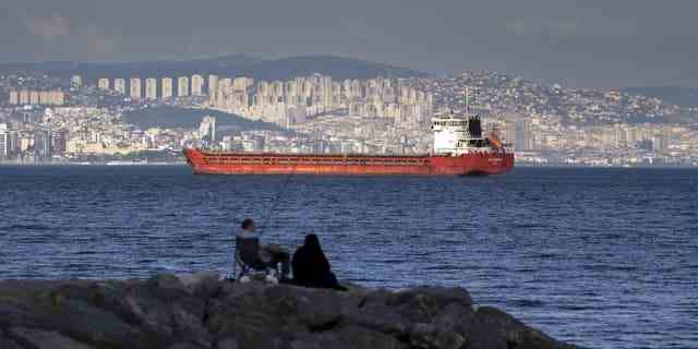 Eine Familie sitzt auf einem Felsen vor einem Frachtschiff, das im Marmarameer ankert, und wartet darauf, am Mittwoch, den 13. Juli 2022, die Bosporus-Meerenge in Istanbul, Türkei, zu überqueren. 