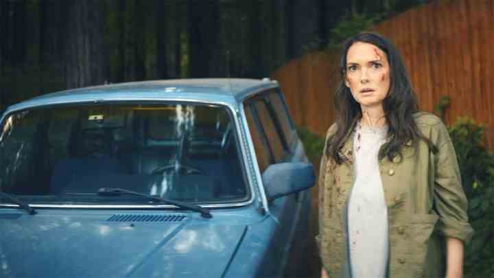Winona Ryder steht in Gone in the Night neben einem blauen Auto.