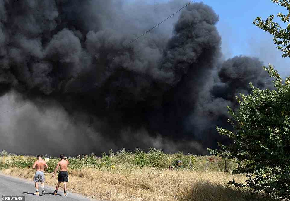 A huge black smoke cloud spreads as round 100 firefighters tackle a blaze in the village of Wennington this afternoon as the heatwave continues