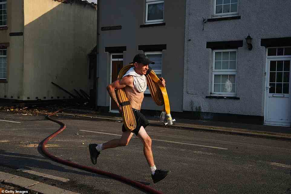 A man runs along a street with a hosepipe on July 19, 2022 in Wennington, England