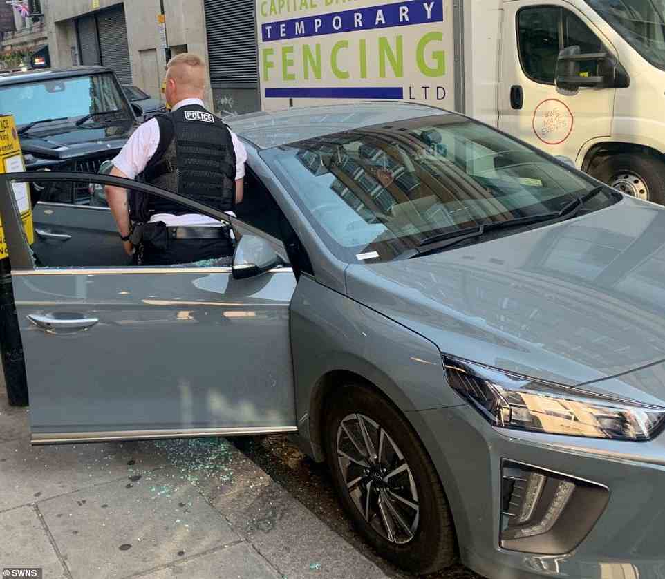An officer stands inside the driver's door of the car with glass shattered over the pavement after having to break inside