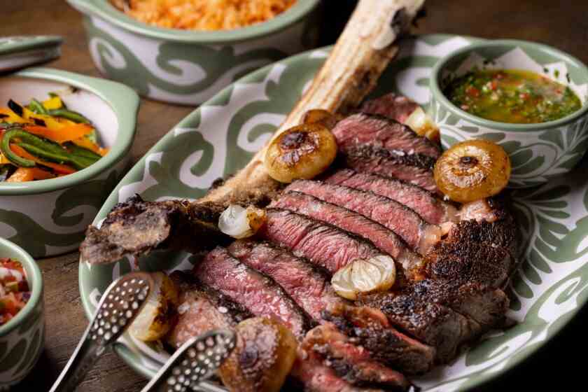 Ein Foto von geschnittenem Steak mit Knochen auf einer Platte, versetzt mit ganzen gekochten Zwiebeln.