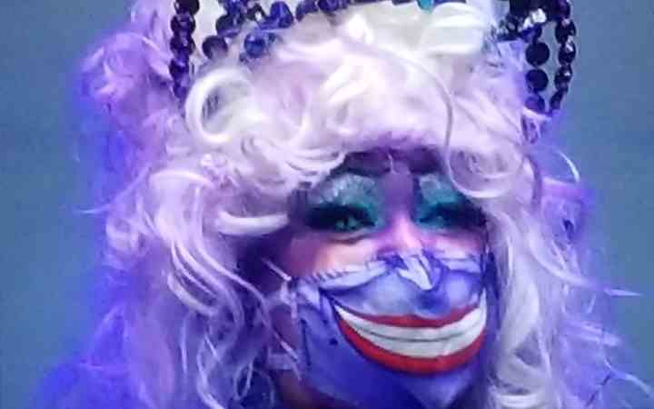 Eine Cosplay-Kandidatin verwendet ihre Maske, um ihr Ursula-Cosplay zu vervollständigen.