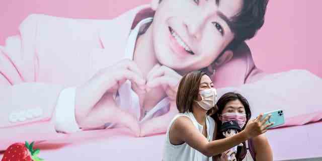 Zwei Frauen machen ein Selfie vor einer Werbetafel, die ein Porträt von Anson Lo zeigt, einem Mitglied der Cantopop-Boyband "Spiegel," in Hongkong.