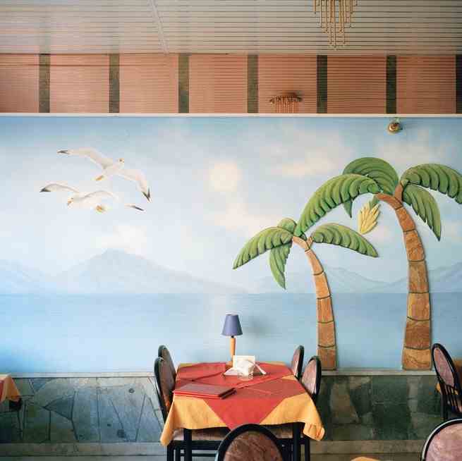 ein Esstisch vor einem Gemälde einer Meeresszenerie mit Palmen und Möwen