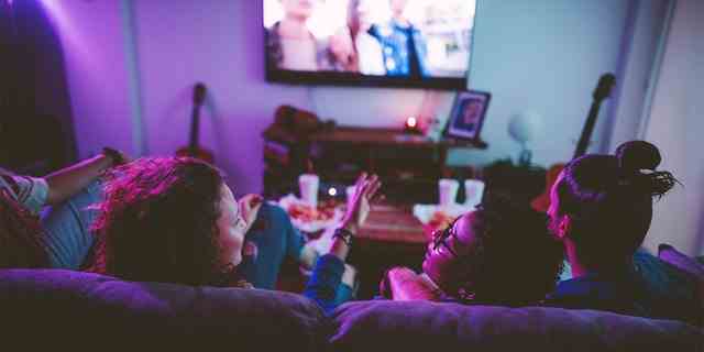 Freunde entspannen sich auf dem Sofa im Wohnzimmer und schauen sich Filme im Fernsehen an