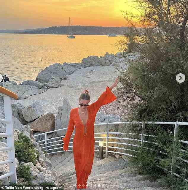 Die Schönheit brutzelte in einem orangefarbenen Kleid für ein atemberaubendes Sonnenuntergangsbild auf einer ihrer vielen extravaganten Reisen
