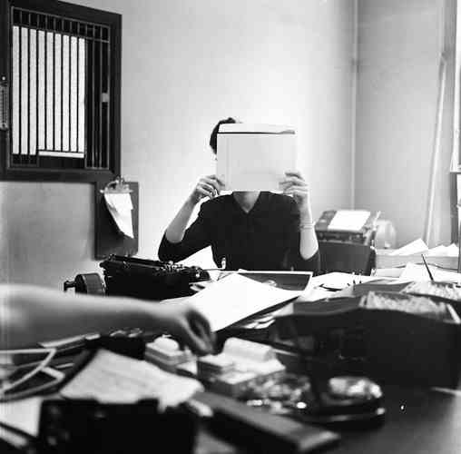 Schwarz-Weiß-Foto einer Person, die an einem vollgestopften Schreibtisch arbeitet