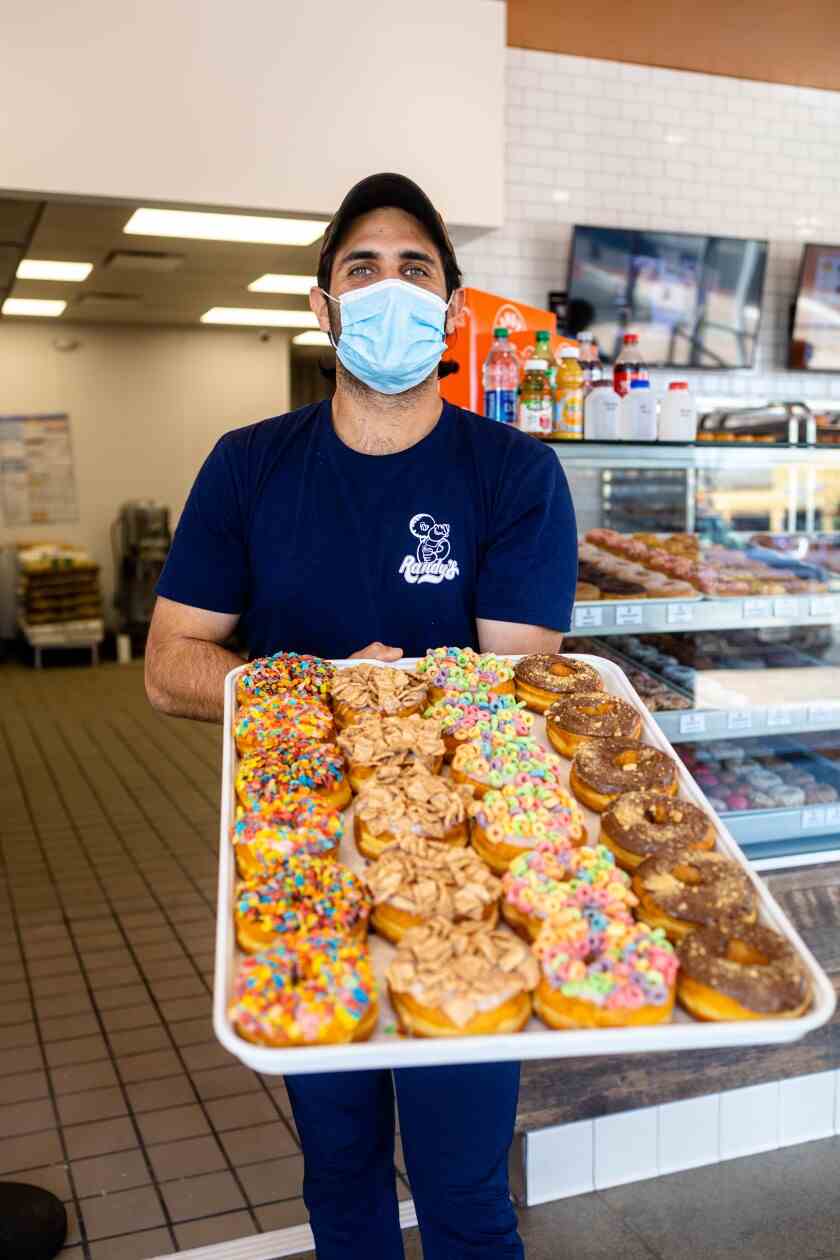 Ein Foto von Kavon Azir, der ein Tablett mit bunten Donuts in seinem neuen Standort von Randy's Donuts hält.