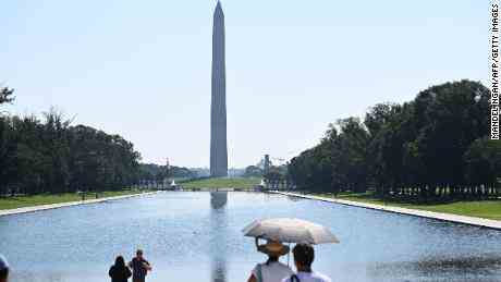 Menschen benutzen einen Regenschirm, um sich vor der Sonne zu schützen, während sie am Samstag das Washington Monument in Washington, DC, betrachten
