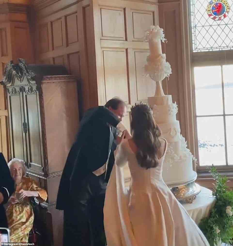 Das Paar gab vor seinen Freunden an, als sie sich bemühten, eine riesige weiße Hochzeitstorte auf einem riesigen silbernen Ständer zu schneiden