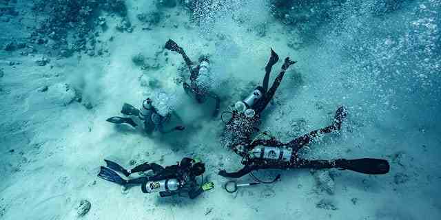Taucher werden gezeigt, wie sie auf dem Meeresgrund nach vergrabenen Schätzen graben – dem Ort eines Schiffswracks auf den Bahamas.