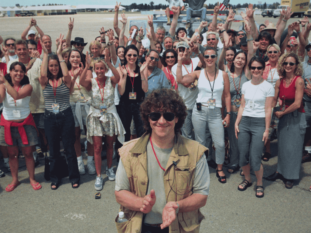 Ein junger Michael Lang blickt in die Kamera, während er vor einer Gruppe von Menschen steht, Trainwreck Woodstock 99