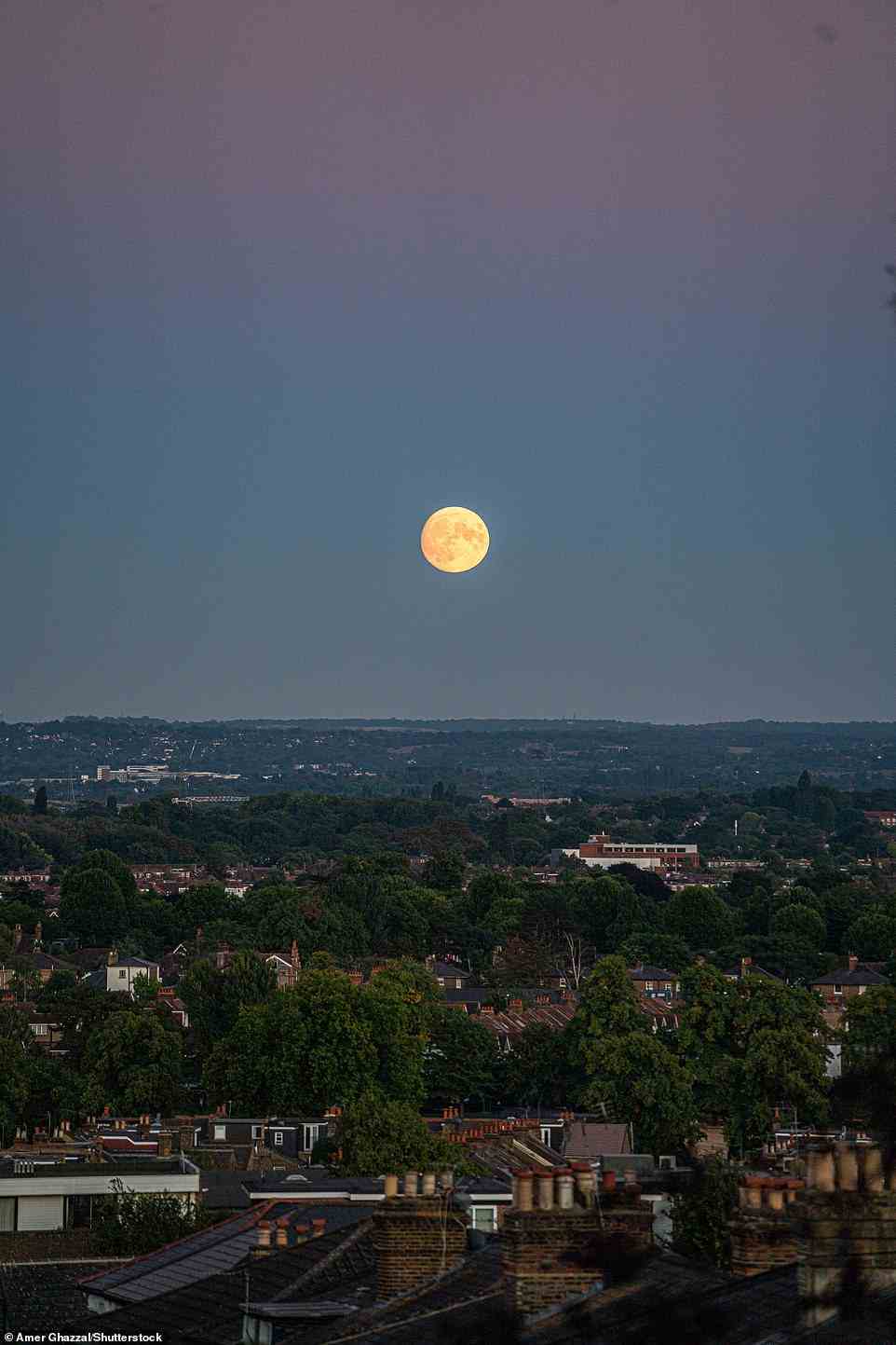 The moon rises above the landscape in Wimbledon south west London at sunset on August 10