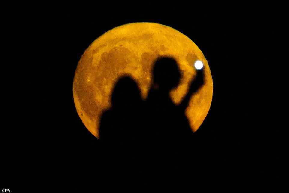 A couple watch the Sturgeon supermoon, the final supermoon of the year, rise over a hill in Ealing, west London on Thursday, August 11, 2022