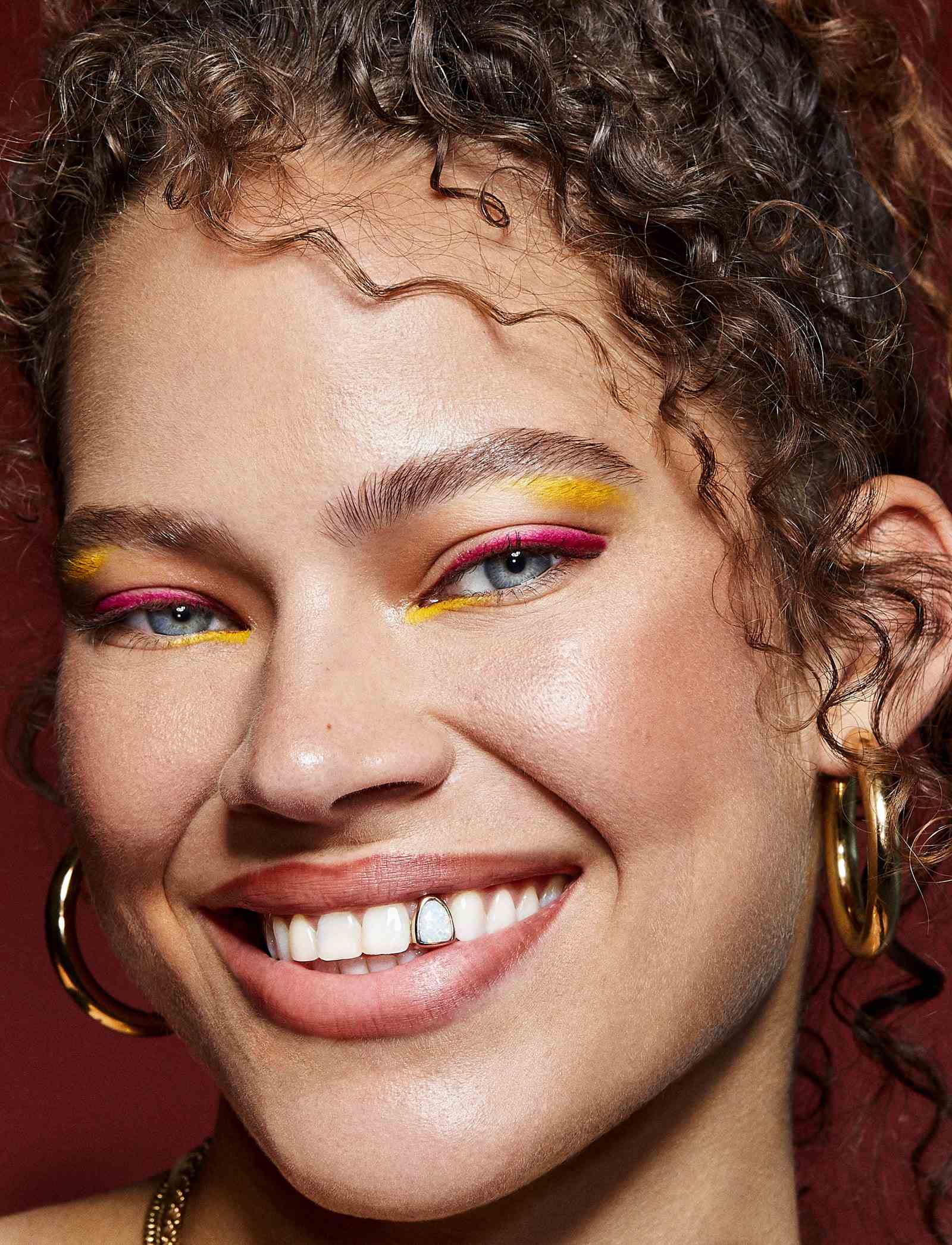 Porträt eines Models mit hellgelbem und pinkfarbenem Liner, das in die Kamera lächelt, um ihre Opalzahnkappe zu zeigen