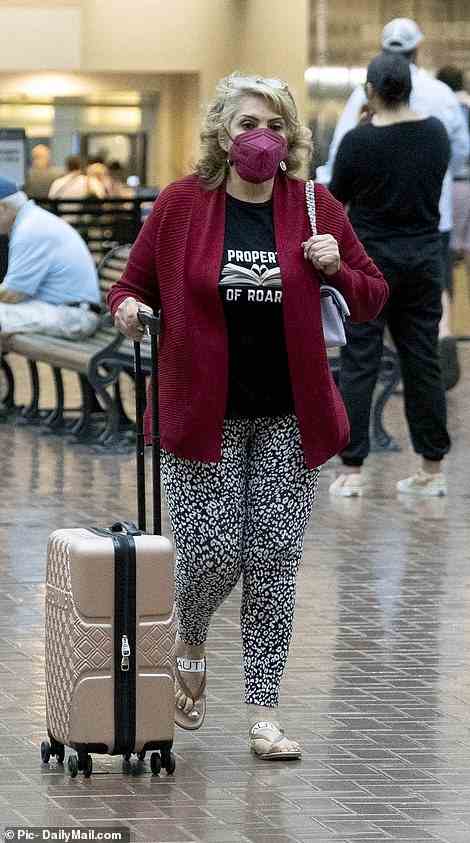 Her mother was seen at the airport in a red cardigan and sandals, pulling a small pink suitcase