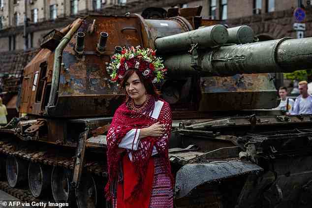 Eine Frau in ukrainischer Nationaltracht posiert vor einem von Putins Kampfpanzern