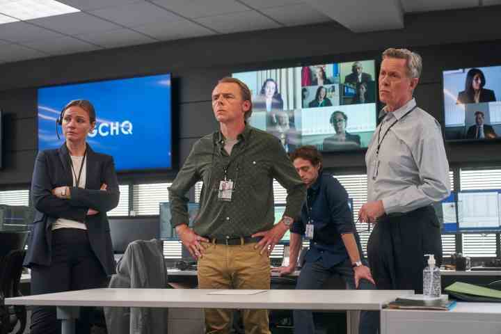 Simon Pegg und eine Gruppe von Menschen stehen in einer Szene aus „Der unerklärte Krieg“ und starren auf einen Bildschirm.