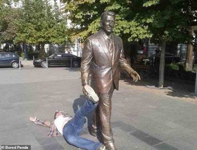 Du kommst mit mir!  Die Statue von Ronald Reagan beschloss, diesen Mann an seinem Schuh durch eine Straße in Budapest, Ungarn, zu ziehen