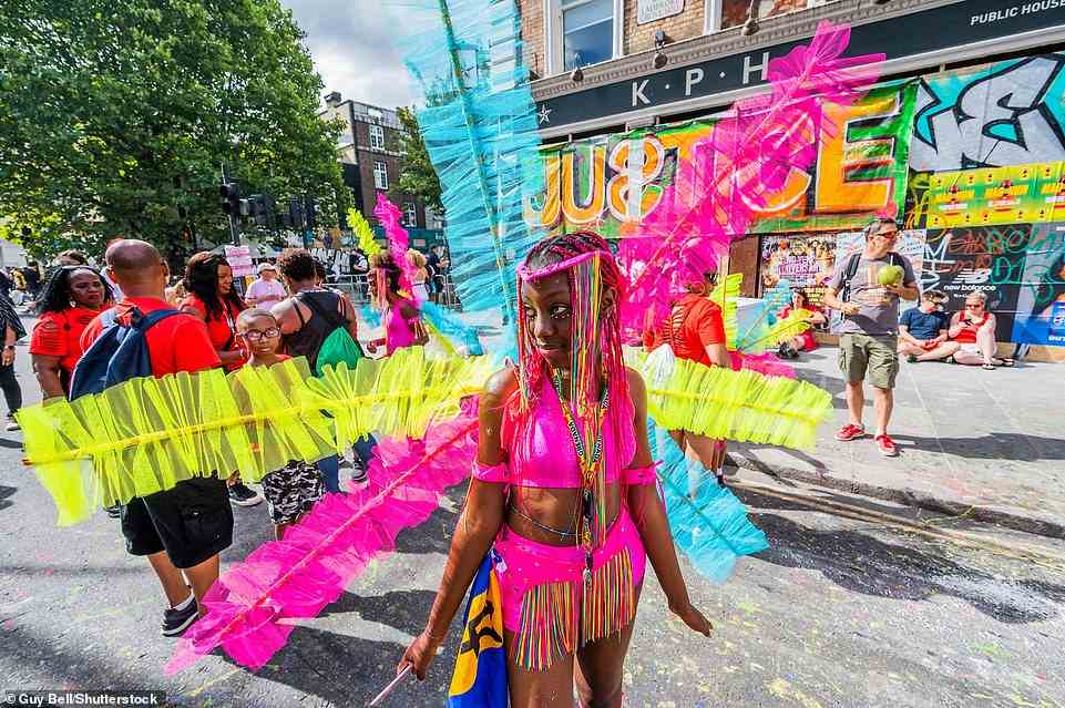 A dancer dressed in neon colours and with jewels adorning her face takes a break to watch other carnival acts