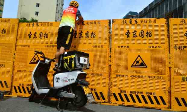 Ein Kurier steht auf einem Elektrofahrrad, um eine Lieferung über eine Barrikade in Sanya in der Provinz Hainan zu machen