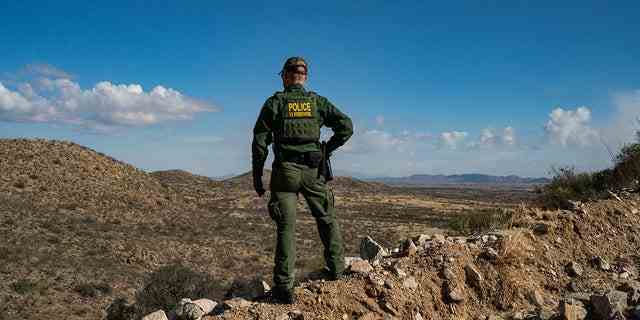 Ein US-Grenzschutzbeamter steht auf einer Klippe und sucht nach Migranten, die am 23. Januar 2022 die Grenzmauer zwischen den USA und Mexiko in der Nähe der Stadt Sasabe, Arizona, überquert haben.