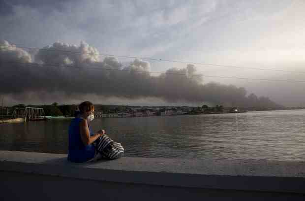 Ein Anwohner sitzt auf der Malecon-Dammmauer, während Rauch vom Feuer im Hintergrund aufsteigt.