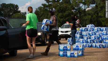 Quad Johnson, Mitte, trägt am Mittwoch Pakete mit abgefülltem Wasser zu Autos an einer Wasserverteilungsstelle im Grove Park Community Center in Jackson, Mississippi.
