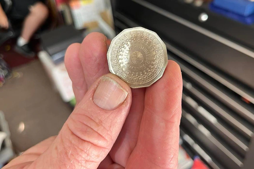 Eine Nahaufnahme der Hand eines Mannes, der eine 50-Cent-Münze hält.