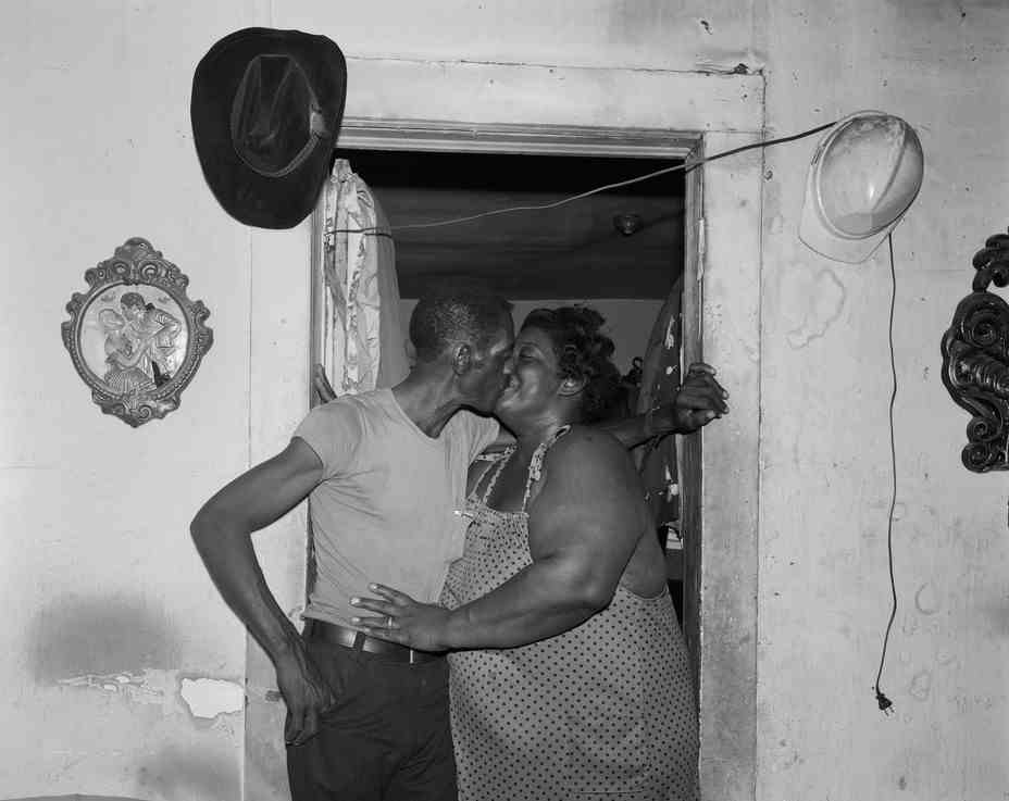 Ein Paar, das sich in einem Türrahmen küsst, mit einem Cowboyhut und einem Schutzhelm, die an der Wand hängen