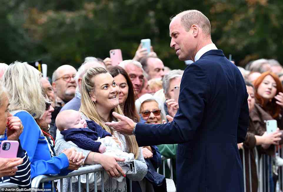 Prince William gestures as he speaks to a young woman, clutching a baby, as the crowds assemble at Sandringham