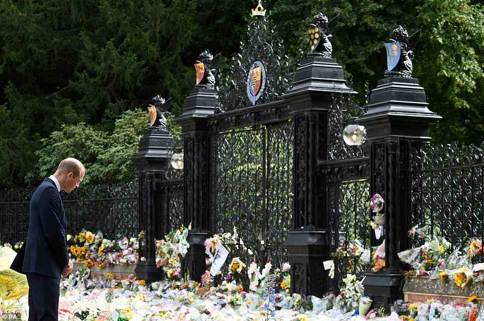 Prince William cuts a forlorn figure as he looks over the swathes of bouquets left at the gates of Sandringham House