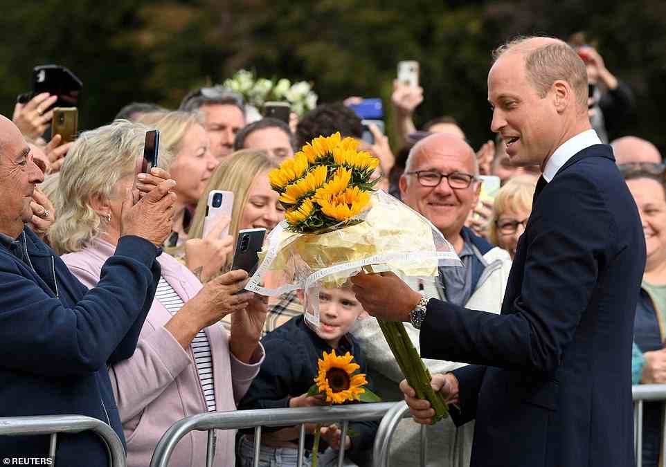 William, Prince of Wales, holds a floral tribute as he meets people gathered outside Sandringham Estate