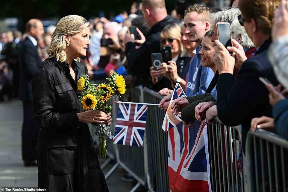 Sophie receives sunflowers from a crowd member standing behind a metal barrier draped in a Union flag