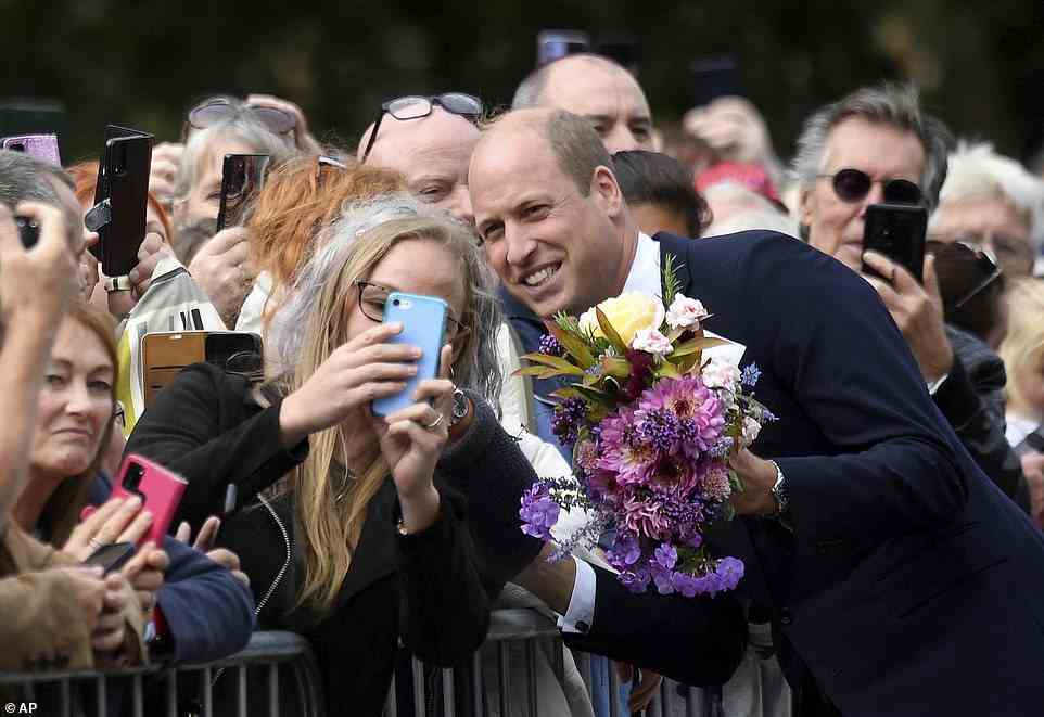 William holds a bouquet of flowers as he speaks to a woman outside Sandringham in Norfolk this afternoon
