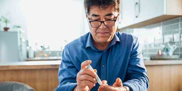 Ein Mann an einem Esstisch in seiner Küche sticht sich mit einem Glaukometer in den Finger, um seinen Blutzuckerspiegel zu testen.  Diabetes entwickelt sich am häufigsten bei Menschen über 45 Jahren, aber heute erkranken auch mehr junge Erwachsene, Teenager und Kinder daran, sagen Gesundheitsbehörden.