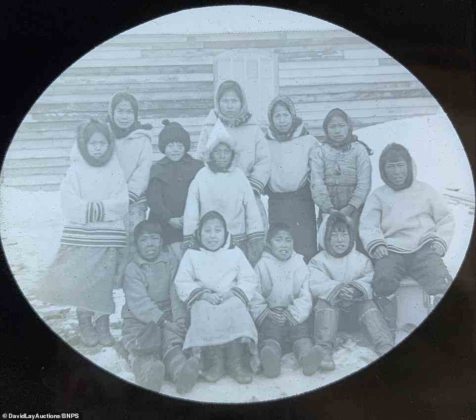 A portrait of local children wearing traditional clothing as they sit and stand on the frozen ground in Labrador