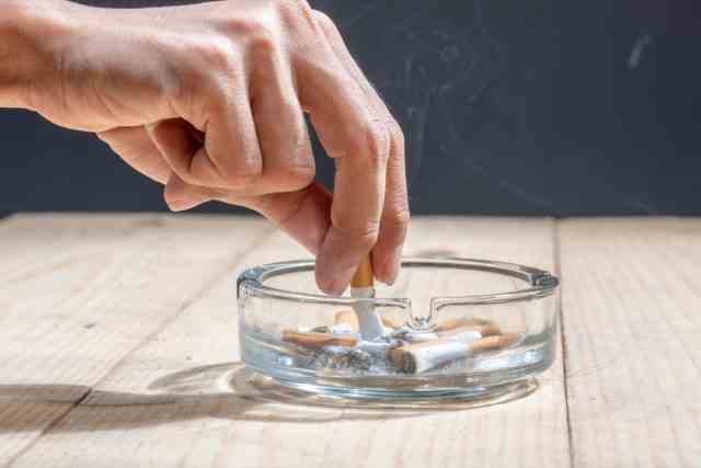 Hand drückte die Zigarette in einem transparenten Aschenbecher auf einem Holztisch aus